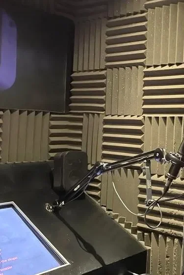 The treated recording booth: foam panels, a microphone on a boom arm and the script on a screen